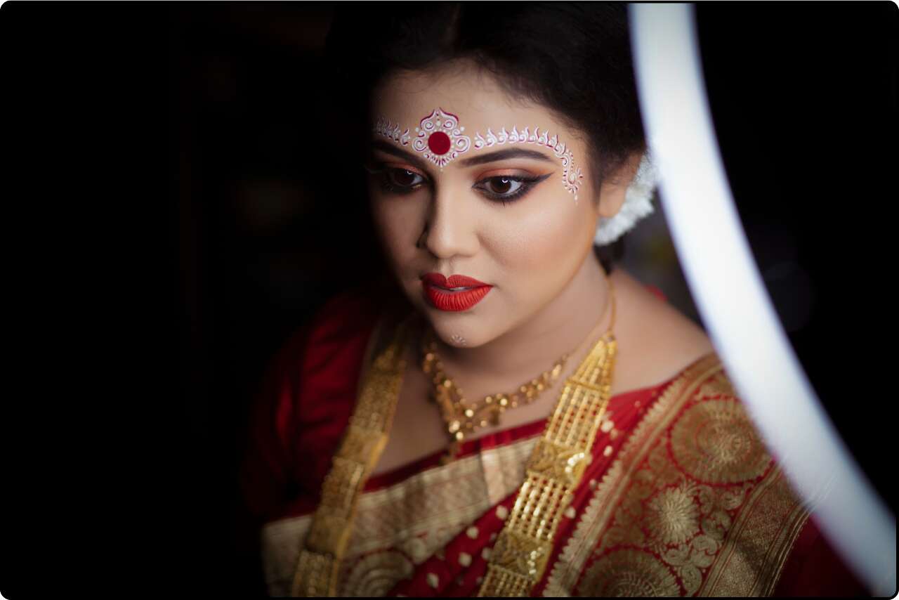 Bengali bride in a red Banarasi saree, with a gold necklace, earrings ready for her wedding rituals.